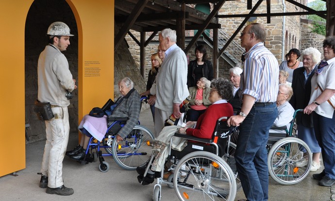 Besucher*innengruppe mit Rollstuhlfahrern auf dem Zechengelände Besucher*innengruppe mit Rollstuhlfahrern auf dem Zechengelände