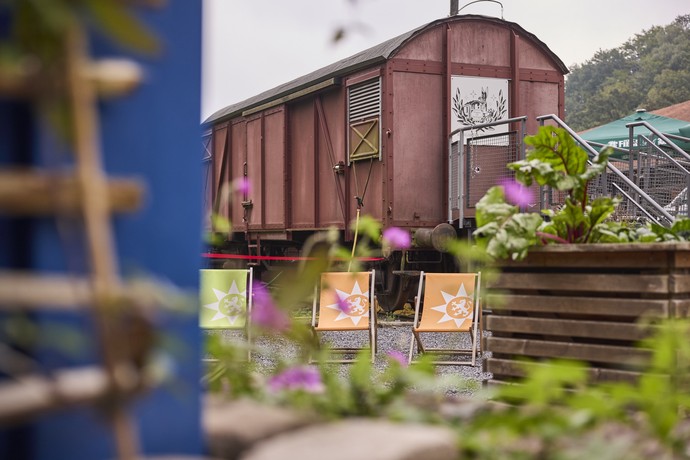 Blick auf den Gastronomiebereich mit Liegestühlen und altem Bahnwaggon