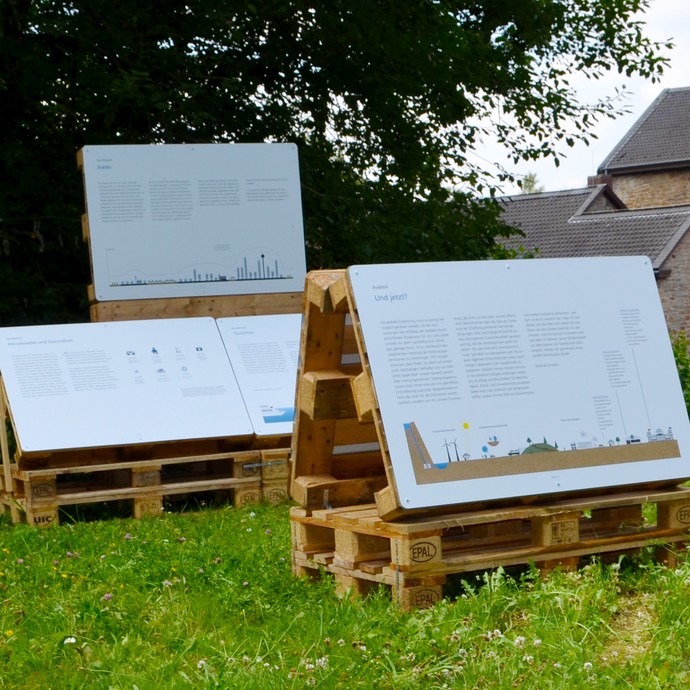 Blick auf drei Palletten der Ausstellung auf grüner Wiese. (vergrößerte Bildansicht wird geöffnet)