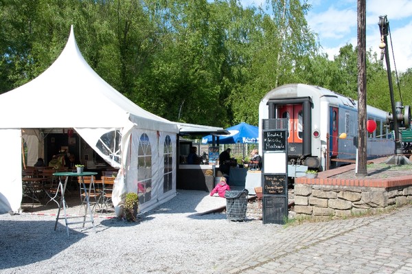 Weißer Zeltpavillon, eine Eisennbahnwagon und ein kleiner Biergarten - Blick auf die Gastronomie auf dem Gelände der Zeche Nachtigall.