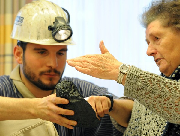 Museumspädagoge zeigt Seniorin ein Stück Kohle.