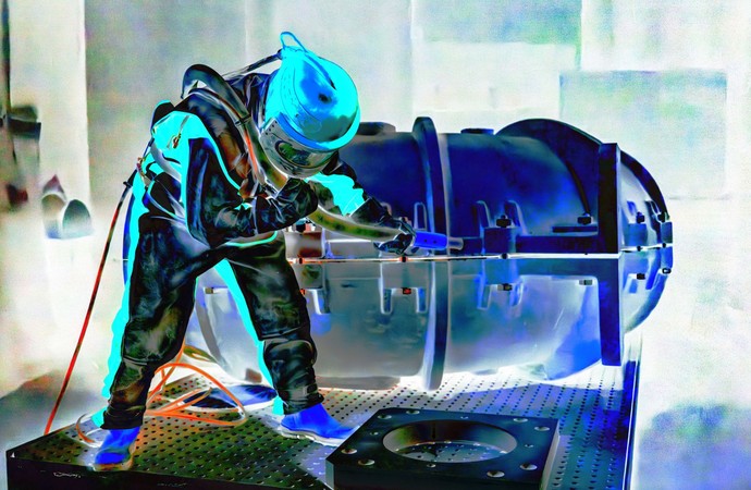 Farblich bearbeitete Fotografie eines Arbeiters in Schutzkleidung beim Bestrahlen einer Werkstücks.