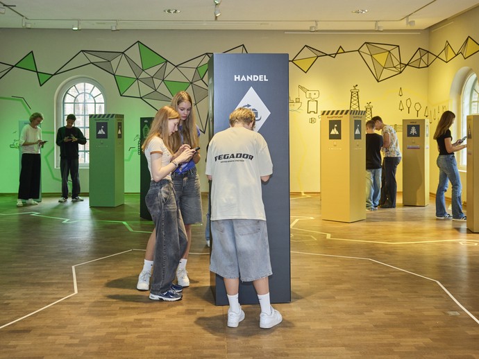 Jugendliche stehen an Stationen der einer Ausstellung zu Rohstoffen.
